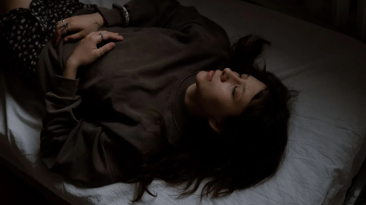 A person lying comfortably on a yoga mat with soft, warm light in the background.