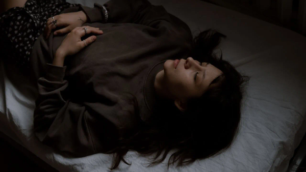 A person lying comfortably on a yoga mat with soft, warm light in the background.