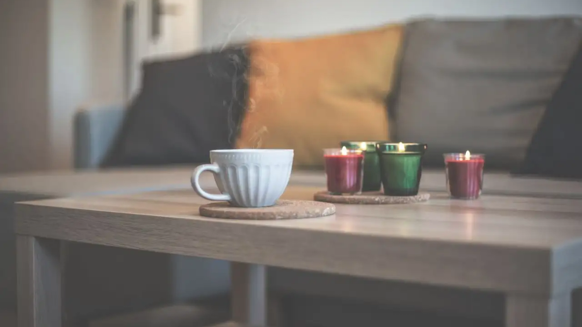 A warmly lit living room in the evening — a candle on the windowsill, a mug of herbal tea on a wooden table, soft cushions on a sofa