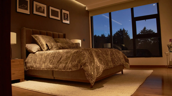 A neatly made bed with soft linen in a cool, dimly lit bedroom.