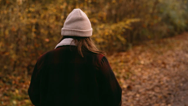 A person walking slowly on a quiet path in soft evening light, among trees.